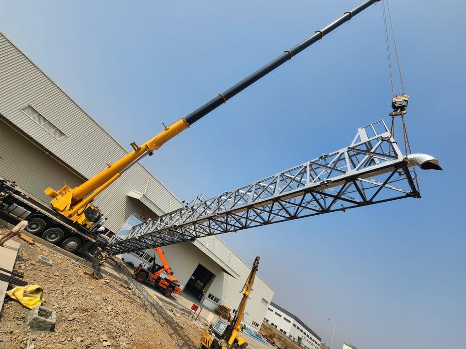 Telescopic crane lifting the complete lattice column off the ground, rain-cap elbow at its head