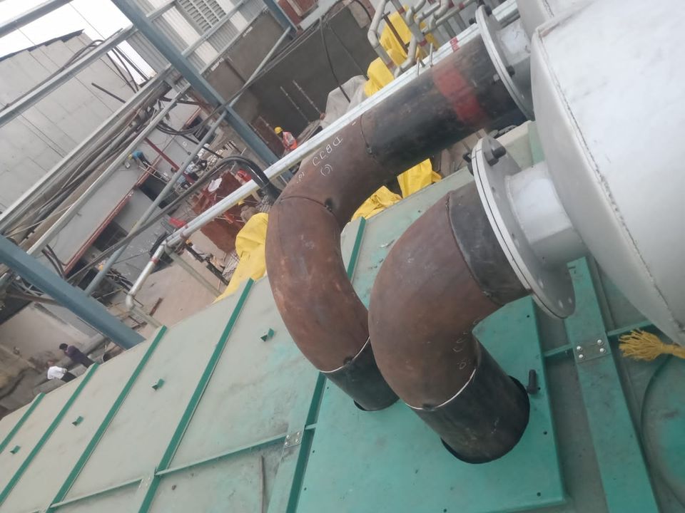 Twin lagged exhaust risers with long-radius bends leaving flanged silencers beside a generator canopy